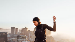 A woman in a black hat by Will & Bear overlooks the cityscape, basking in the warm sunlight.