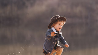 A child in mid-play, laughter captured on their face, wearing an oversized rancher hat in the sunlight.