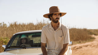 Man wearing a wide brim straw sun hat by Will & Bear in sunny courtyard.