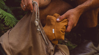 A close-up of a person packing a mustard yellow crushable hat by Will & Bear for travel, showcasing a readiness for adventure.