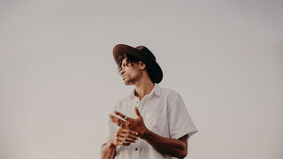 Man in a white shirt and textured brown hat by Will & Bear against a clear sky.
