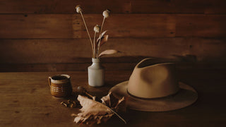 Elegant burnt orange hat by Will & Bear displayed on a rustic wooden surface with decorative leaves.