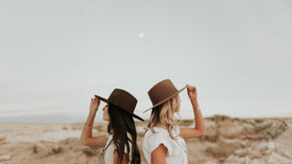 Two women in the desert, side by side, wearing flat brim hats by Will & Bear under a pale sky.