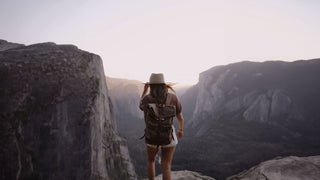 A woman adventurer in a Will & Bear hiking hat stands before a grand valley at dusk, contemplating nature.