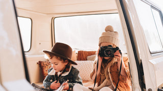 Children in a van dressed in all season clothes, one in a wool hat by Will & Bear, another wearing a wool beanie holding a camera.
