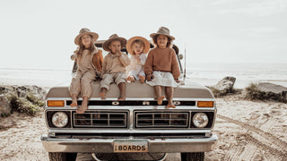 A joyful moment as a parent in a knitted sweater lifts a child wearing a floppy hat by the seaside.