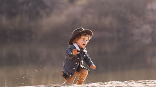 A young child exudes adventure in the outback, wearing an oversized Akubra style hat and a joyous expression.