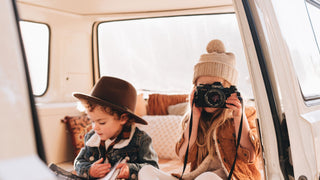 Two children share an affectionate moment on a vehicle's hood, wearing crushable hats suitable for travel.