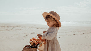 A little girl holding flowers wearing a wide brim sun hat made from straw
