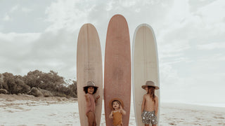 Kids by surfboards on sand, wearing beach hats by Will & Bear, ready for fun.