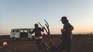 Two men at a desert festival, one wearing a festival hat by Will & Bear