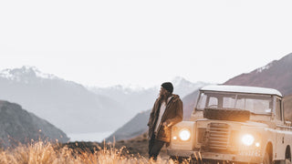 A person by a vintage car, wearing a winter beanie hat by Will & Bear, with mountains in the twilight.