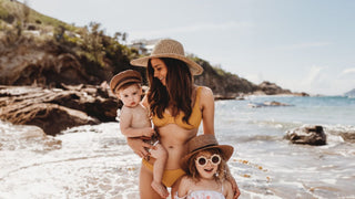 A family with young kids on vacation at the beach wearing straw hats by Will & Bear