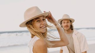 Man and woman in front of vintage car at the beach wearing summer hats by Will & Bear