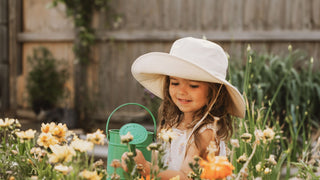 A girl in a white Will & Bear gardening hat watering flowers