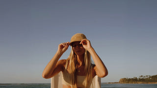 Woman sitting at the beach at sunset wearing a vintage baker cap by Will & Bear
