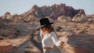 Woman in a black open road hat by Will & Bear with a mountainous desert landscape in the background.