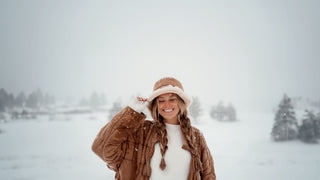 A smiling woman in a winter bucket hat by Will & Bear enjoys the snowfall.