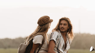 A woman shares a moment with her boyfriend in the countryside, one gazing back while wearing a newsboy or baker cap by Will & Bear.
