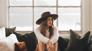 Friends indoors, one adjusting her all-season wool hat by Will & Bear, share a moment.