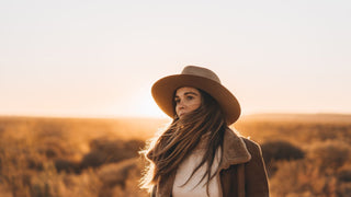 A woman in a warm coat and Akubra style Australian outback hat faces the sunrise in the vast outback.