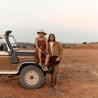 Couple in matching outfits and Anderson Brown hats beside vintage 4WD