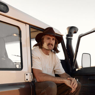 Man sitting in 4WD vehicle wearing Anderson Brown hat and white tee