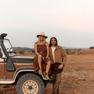 Couple wearing Anderson Cream hats posing beside rugged 4WD in desert setting
