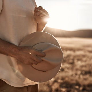Man holding Anderson Cream fedora hat in outstretched hands, close-up detail