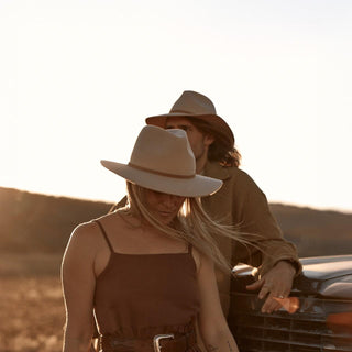 Woman adjusting Anderson Cream fedora with windblown hair in golden light