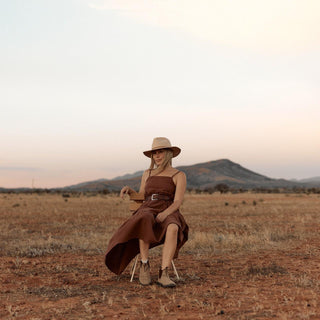 Woman sitting in open field at sunset wearing Anderson Cream fedora
