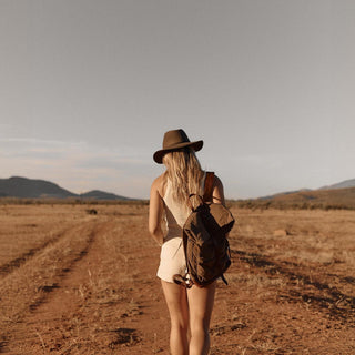 Back view of woman in romper walking with Anderson Olive fedora and backpack