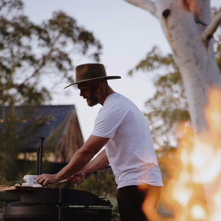 Man grilling outdoors in a Will & Bear Wide Brim Country Hat, captured in warm bushland light.