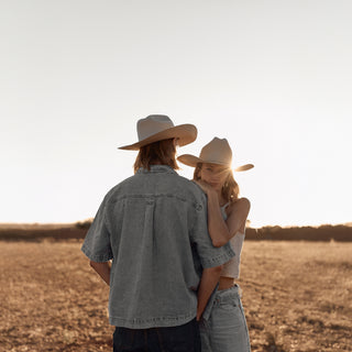 A couple walking through dry grassland at sunset, each styled with a Will & Bear white cowboy hat felt.
