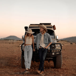 Two travellers resting beside a 4WD, both sporting Will & Bear white cowboy hats felt for sun protection.