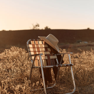White cowboy hat felt by Will & Bear perched on a striped outdoor chair in golden hour light.