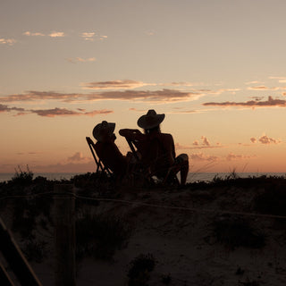 Silhouetted couple at sunset, seated in camping chairs, each wearing the Will & Bear white cowboy hat felt.