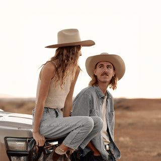 Couple sitting on a car bonnet at golden hour, both wearing the Will & Bear white cowboy hat felt.