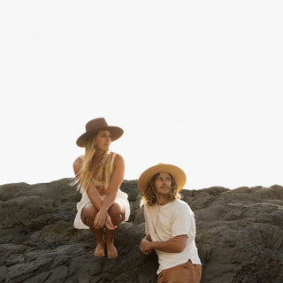 Couple wearing Will & Bear Brown Straw Wide Brim Hats outdoors, enjoying rugged coastline at golden hour