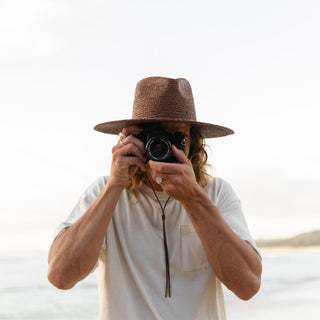 Man in relaxed coastal setting wearing Will & Bear Brown Straw Wide Brim Hat for sun protection and style