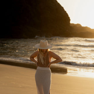 Woman walking along beach wearing Will & Bear straw sun hat at golden hour