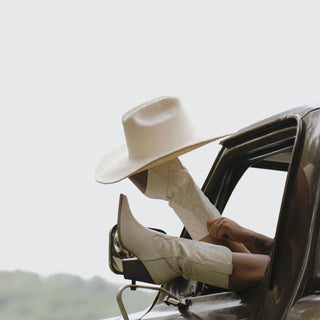 Woman popping her boots through a car window wearing the Will & Bear white straw cowboy hat, embracing the road trip lifestyle.