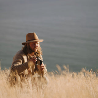 Man wearing Will & Bear Floppy Felt Fedora playing harmonica in open grassland, styled for the outdoors