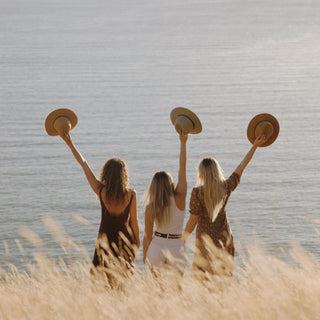 Joyful outdoor moment with Will & Bear Crushable Felt Hats raised by the ocean at sunset