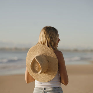 Will & Bear straw sun hat with leather chin strap carried on woman’s back during beach walk