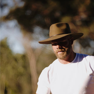 Man wearing Will & Bear Wide Brim Country Hat in the bush, styled with a white tee and rugged outdoor setting.