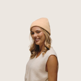 Studio shot of woman smiling in the Will & Bear Bambi Apricot merino wool beanie, a warm and breathable essential.