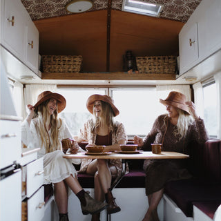 Group of women wearing Will & Bear Camp Bodhi Carob recycled hemp bucket hats enjoying a cosy moment inside a vintage camper.