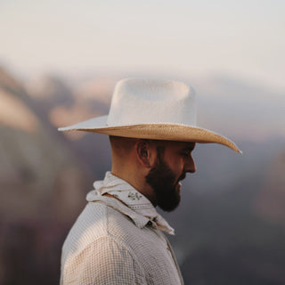 Side view of man wearing the Will & Bear white straw cowboy hat with a rugged desert backdrop.