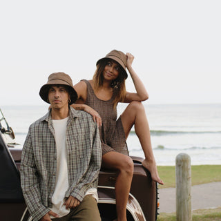 A couple wearing Will & Bear removable string bucket hats at the beach, enjoying the coastal view.